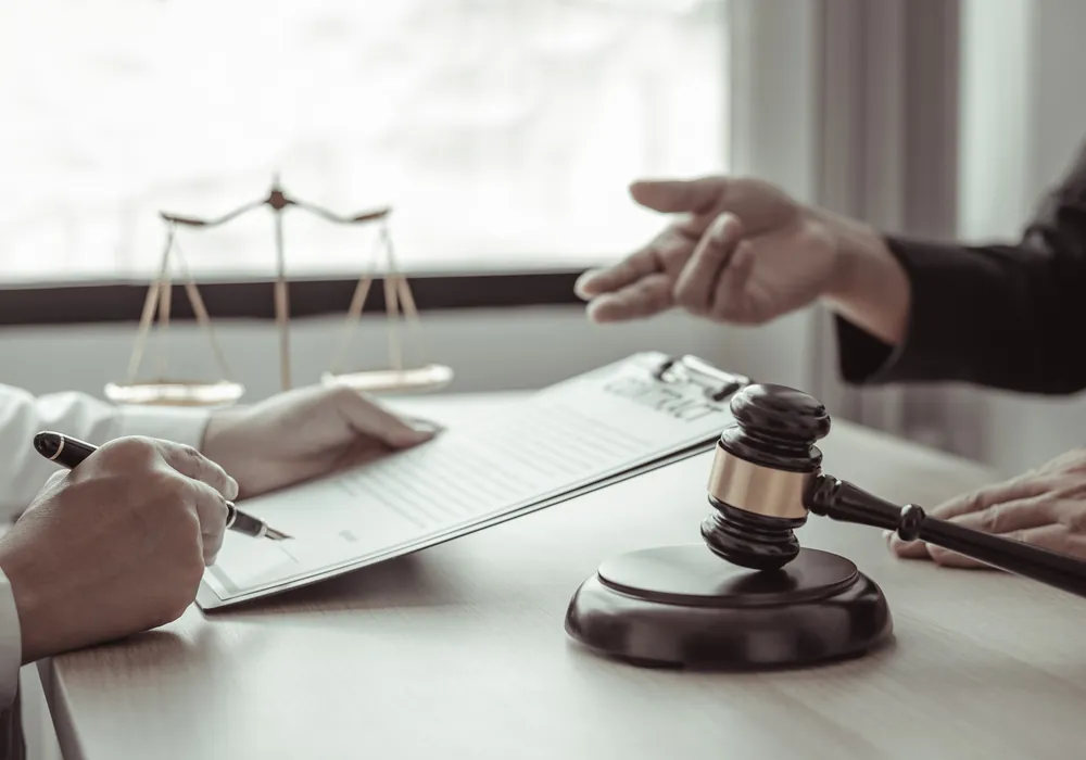 An attorney and client reviewing and signing a contract beside a gavel and scales of justice