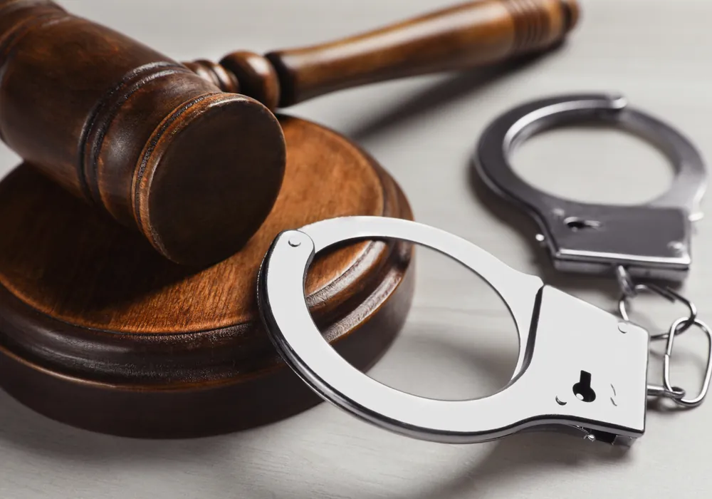 A wooden gavel and a pair of handcuffs on a white surface