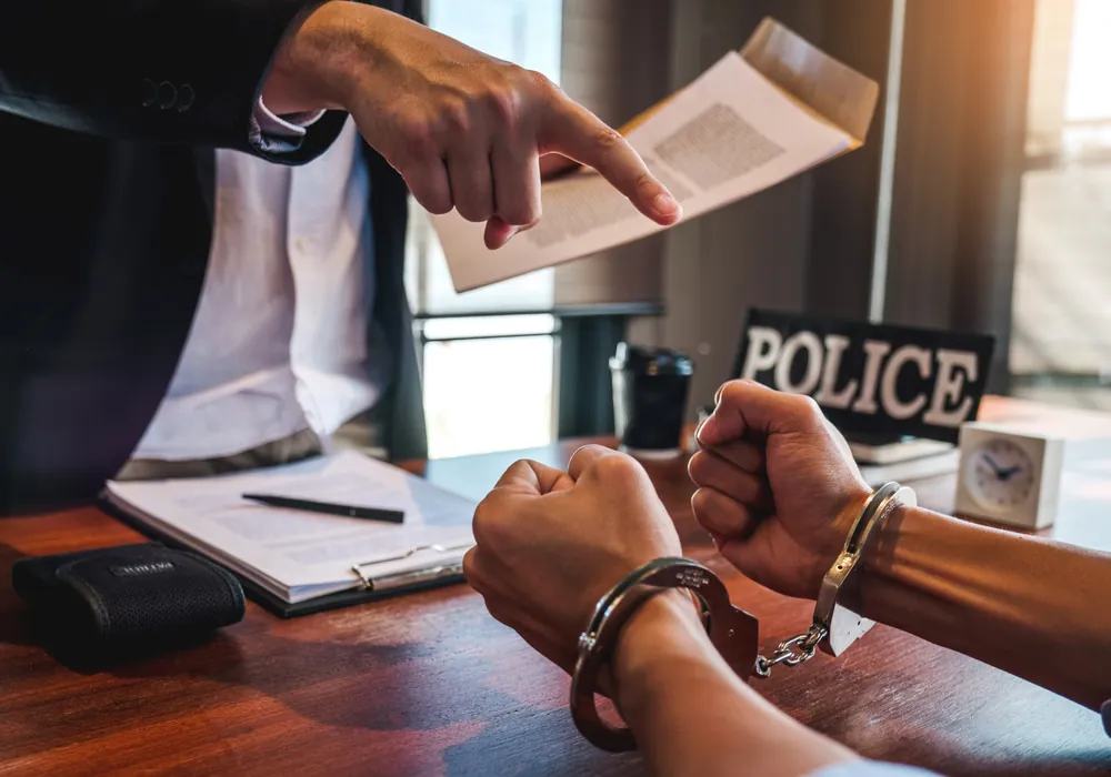 A handcuffed person at a police interview table as an officer points to a document