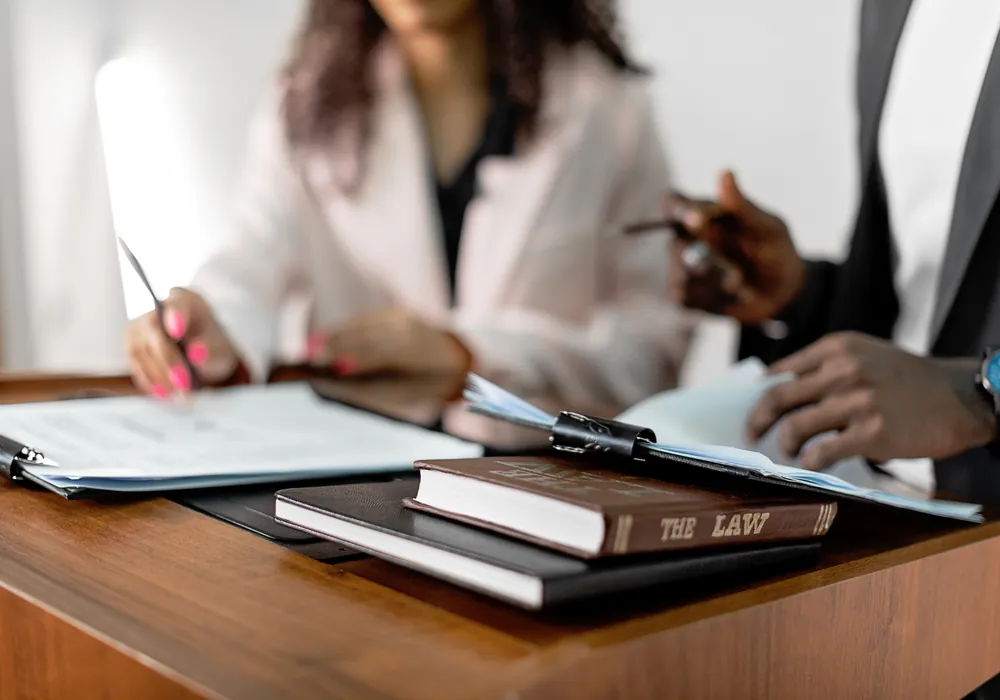 Two people reviewing paperwork at a desk beside a book titled The Law