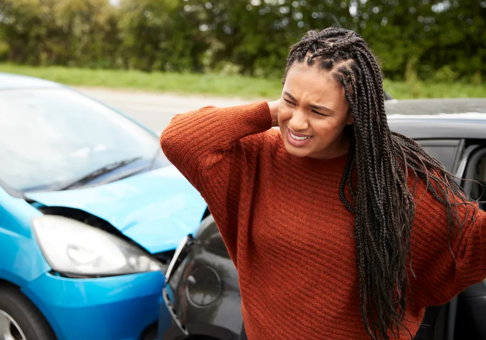A woman holding her neck in pain beside two cars damaged in a collision
