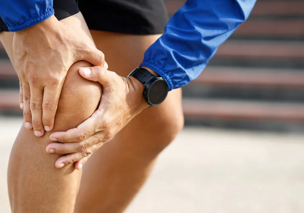 A runner gripping an injured knee on outdoor steps